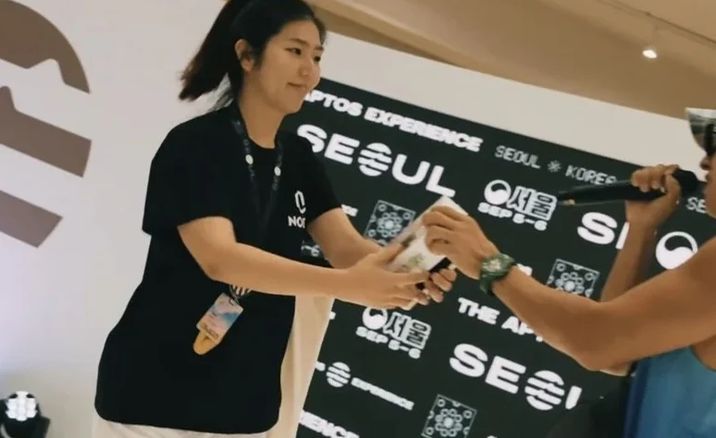 서울 Aptos Experience 부스에서 방문객에게 물건을 건네는 직원
