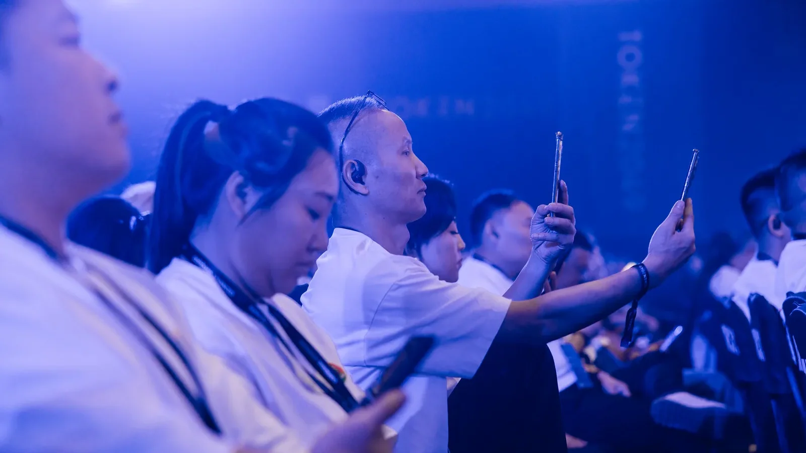Audience filming a main-stage session in blue light, TOKEN2049 Singapore 2025 · editorial context
