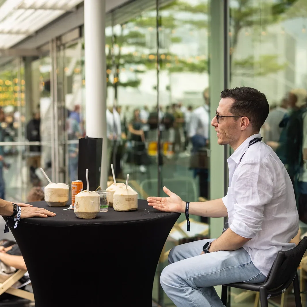 Attendee explaining across a standing table, TOKEN2049 Singapore 2025 · editorial context